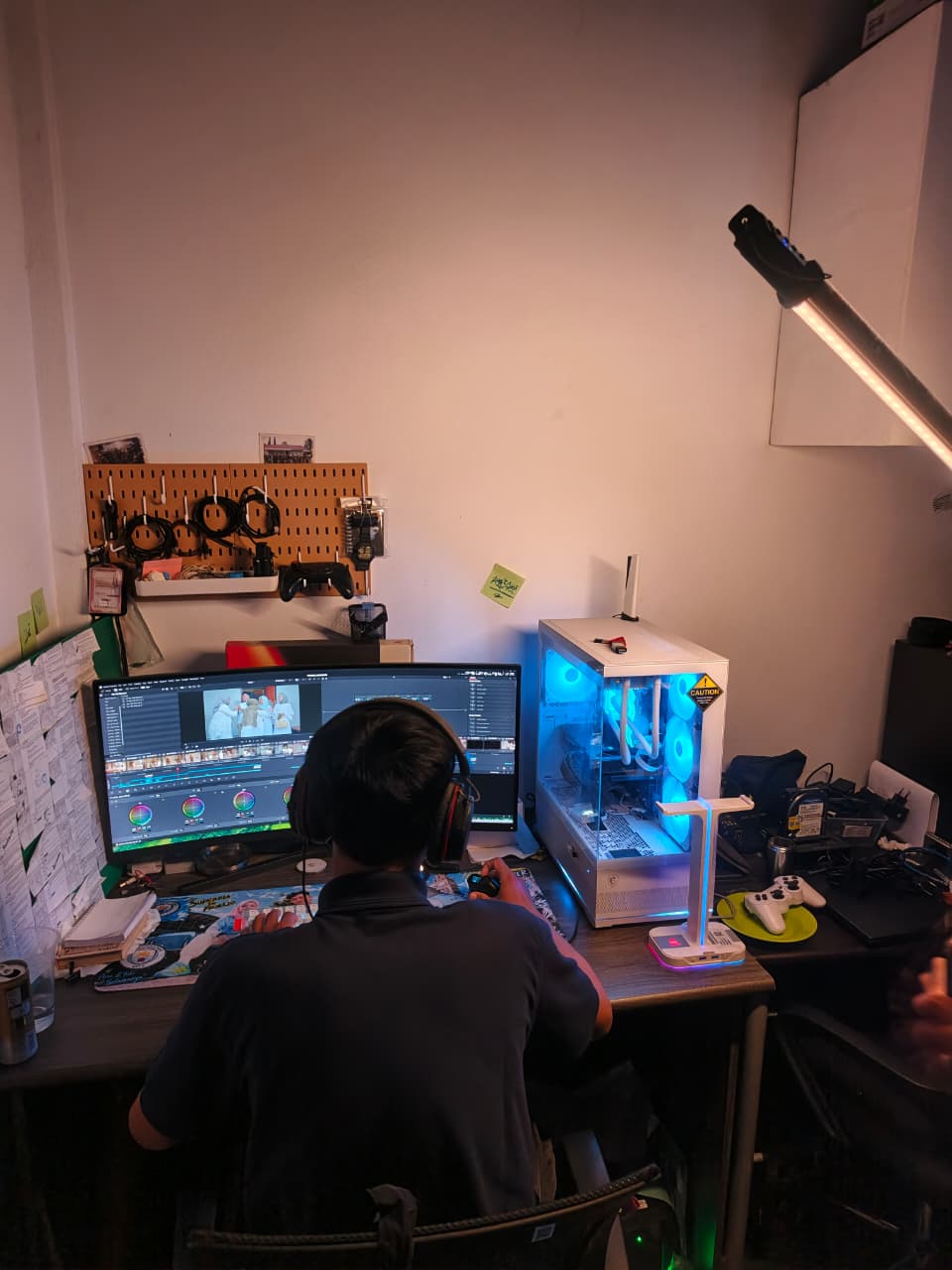 Video editor working at a desk with a widescreen monitor and illuminated computer